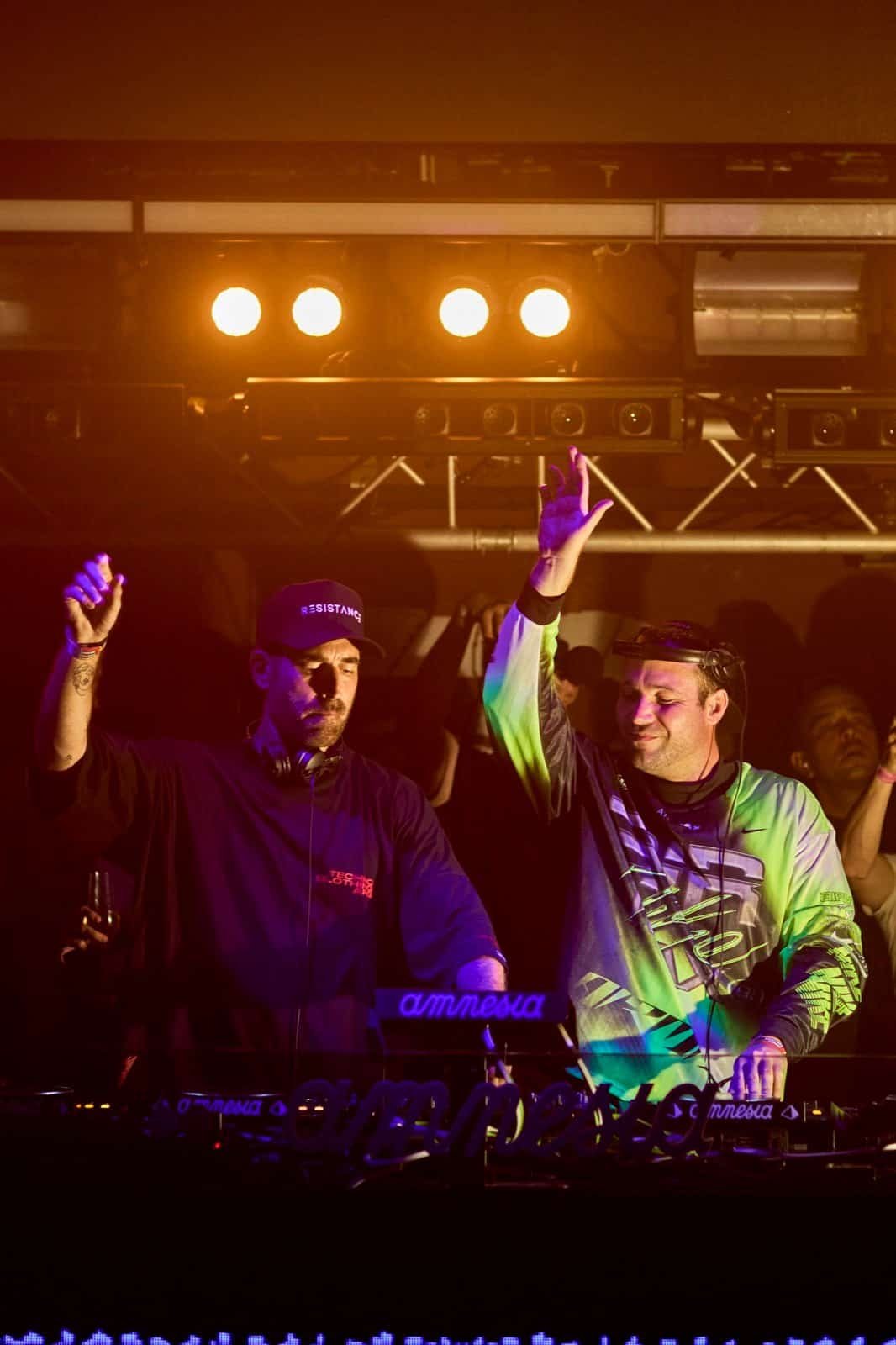 Two DJs raise their hands behind the Amnesia booth during the RESISTANCE Ibiza 2026 opening party
